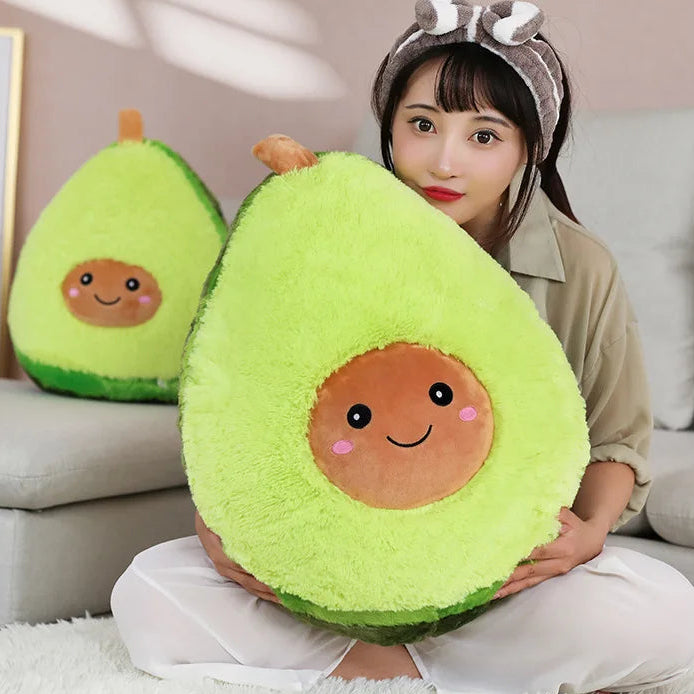 Person holding a kawaii plush avocado toy with a smiling face, sitting on a couch.