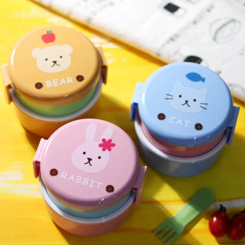 Three colorful kawaii food containers with animal-themed lids on a yellow surface.