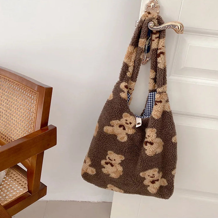 Brown kawaii teddy bear patterned bag hanging on a white wall next to a wooden chair.
