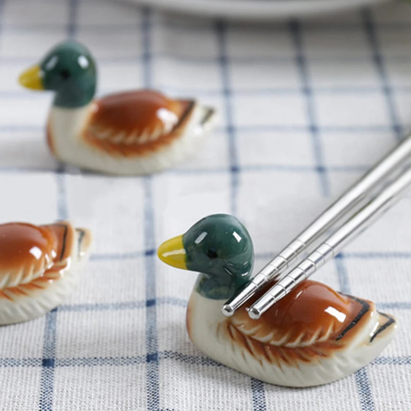 Two ceramic duck-shaped kawaii chopsticks holders on a checkered tablecloth.