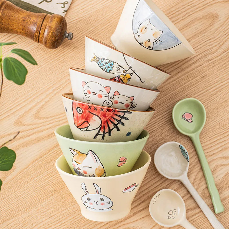 Set of ceramic kawaii ramen bowls and spoons with animal illustrations on a wooden surface