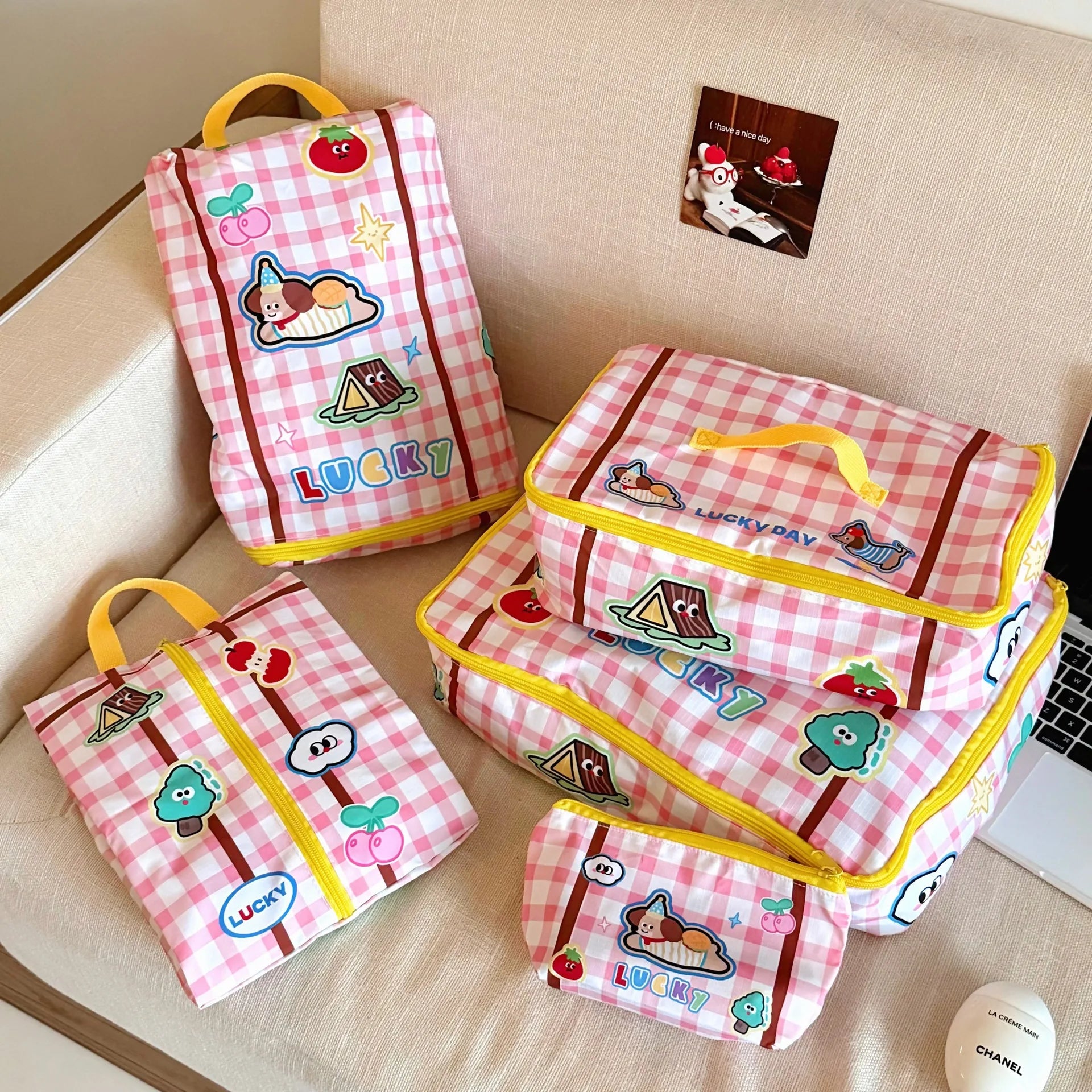Set of pink checkered bags with Kawaii cartoon designs on a beige couch.