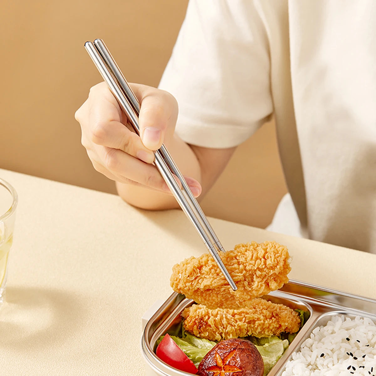 Person using metal kawaii utensils to eat fried chicken and vegetables from a bento box.