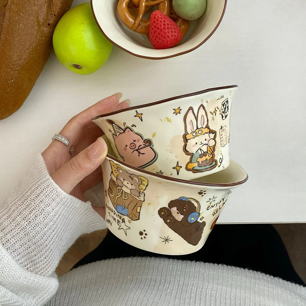 Two ceramic kawaii ramen bowls with cartoon designs held by a hand, with fruits in the background.