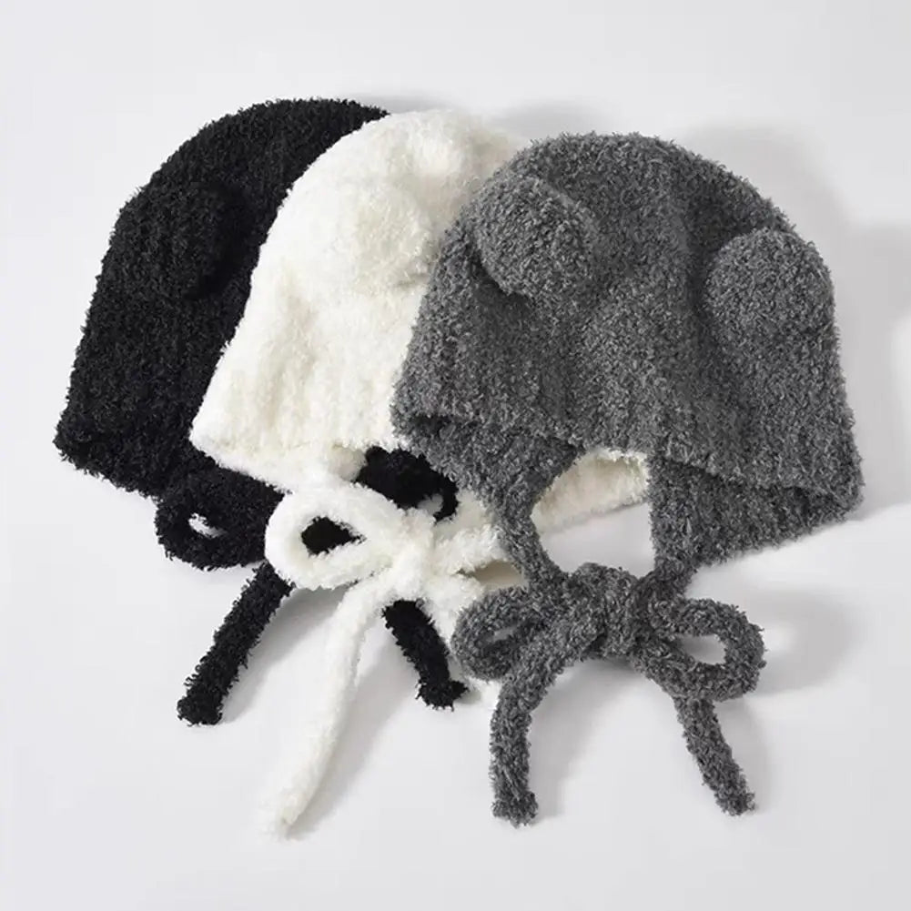 Three fuzzy Kawaii beanies in black, white, and gray on a light gray background