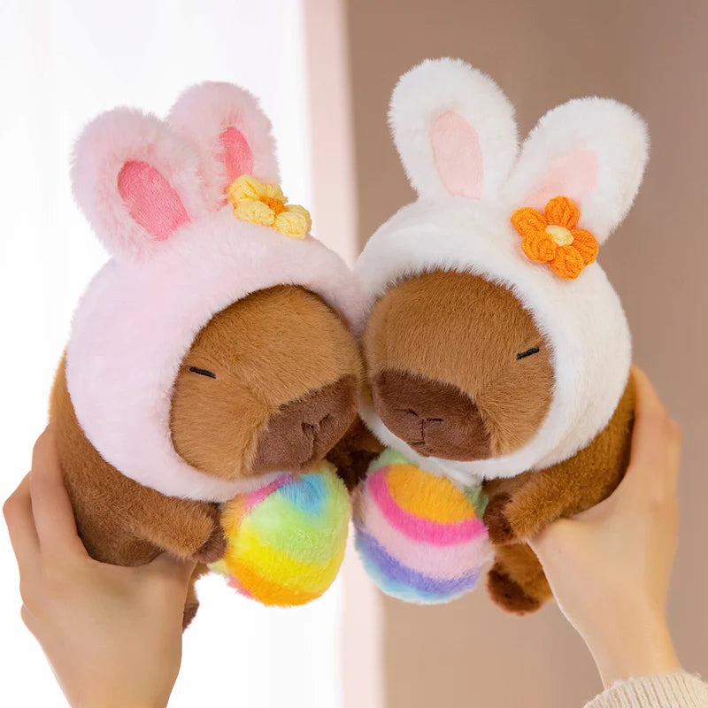 Two kawaii plush toys resembling bunnies with colorful feet held by a person against a neutral background.