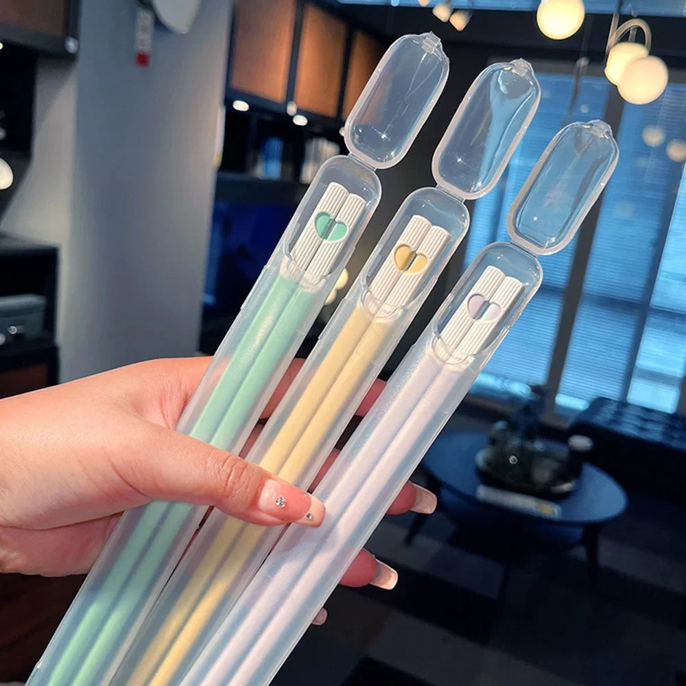 Hand holding a set of colorful kawaii chopsticks with clear cases in an indoor setting.