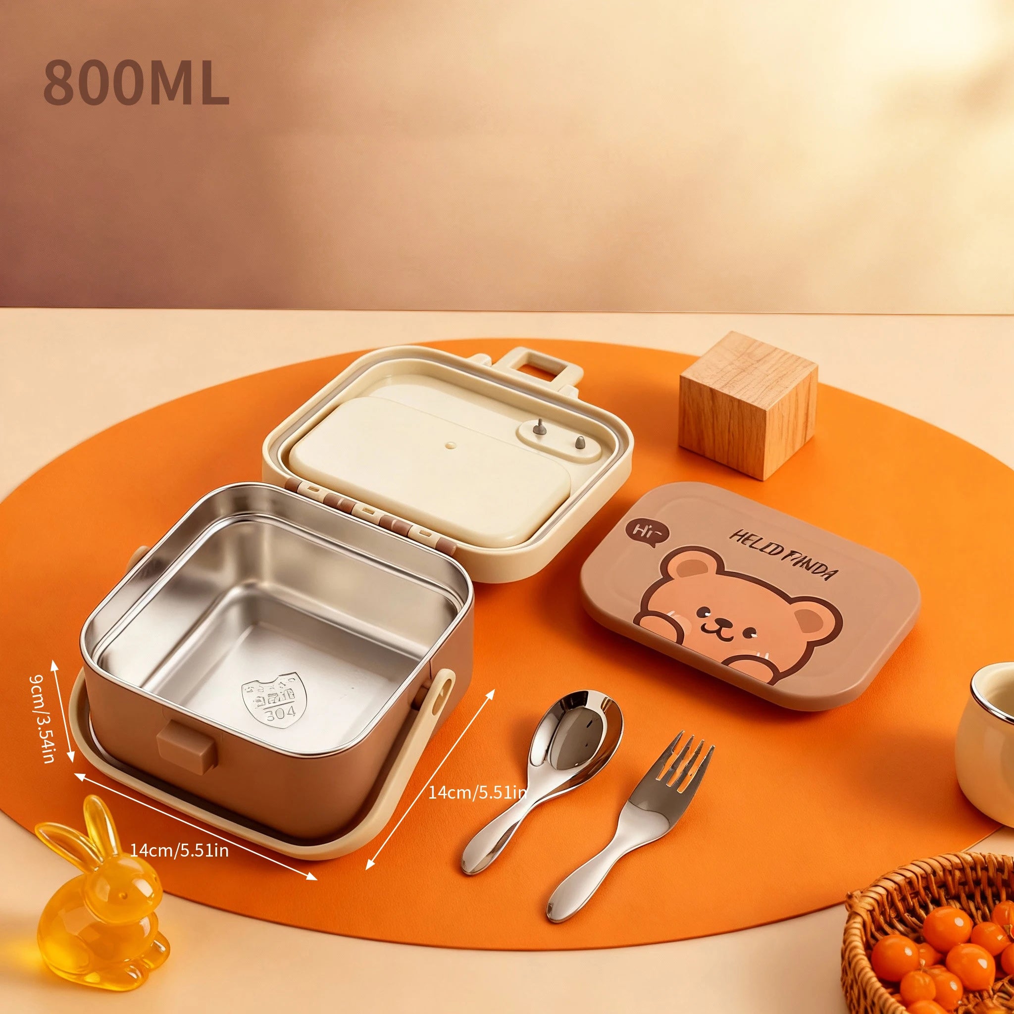 Stainless steel kawaii lunch box with bear design, spoon, fork, and small wooden block on an orange mat.