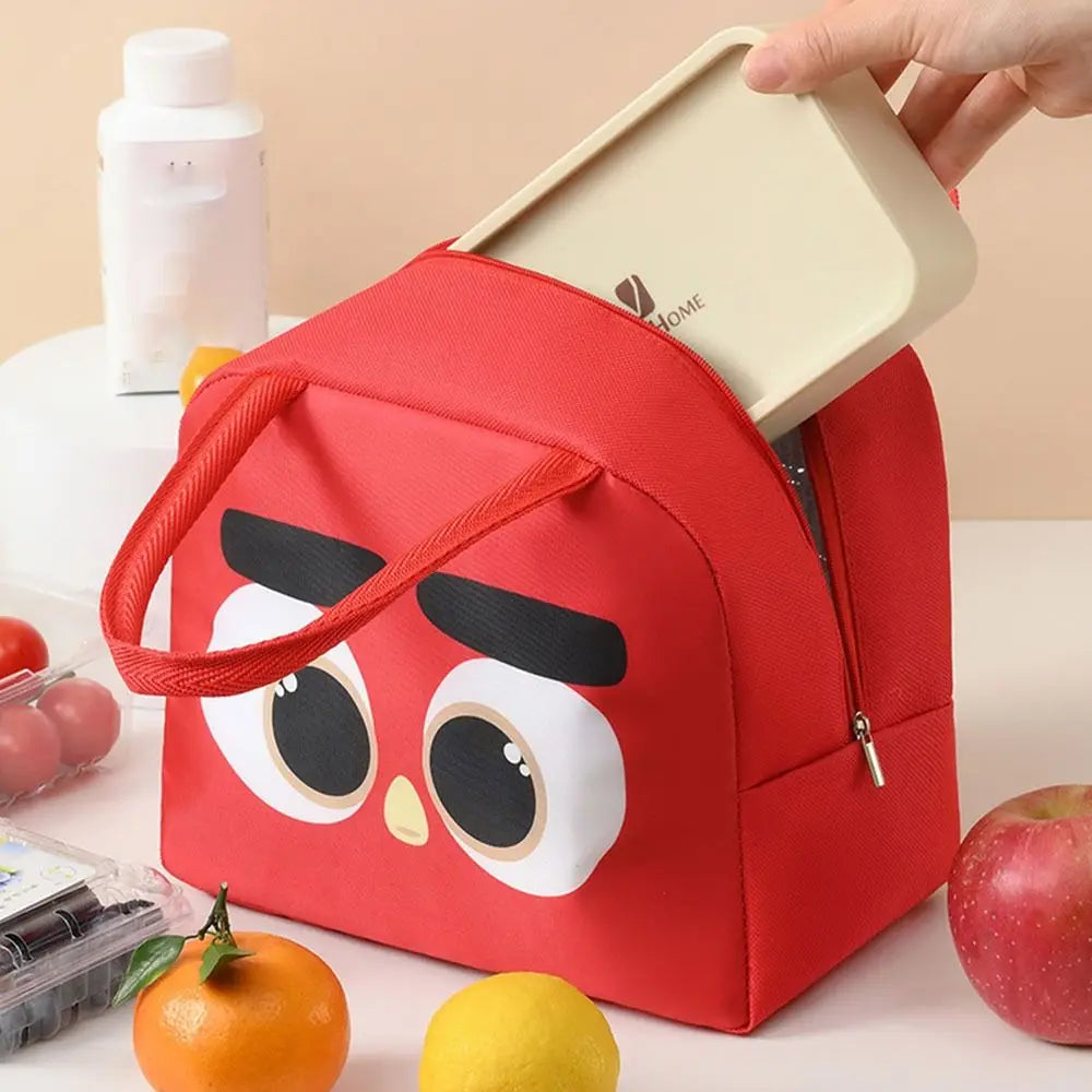 Red kawaii lunch bag with cartoon face design on a table with fruits and a bottle.