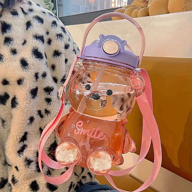 Clear bear-shaped kawaii water bottle with pink accents and 'Smile' text, placed on a textured surface.