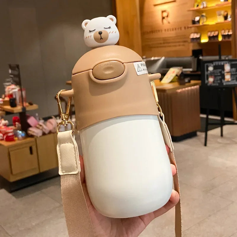 Cute bear-shaped kawaii water bottle with a strap held in a hand, blurred indoor background