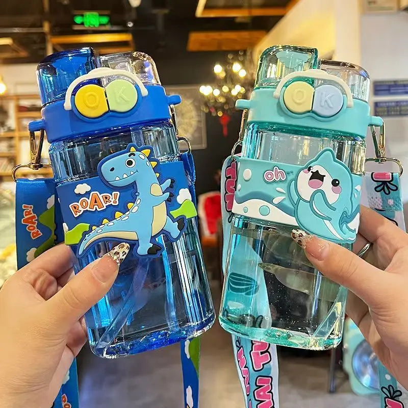Two children's kawaii water bottles with dinosaur and shark designs held by hands in a store setting.