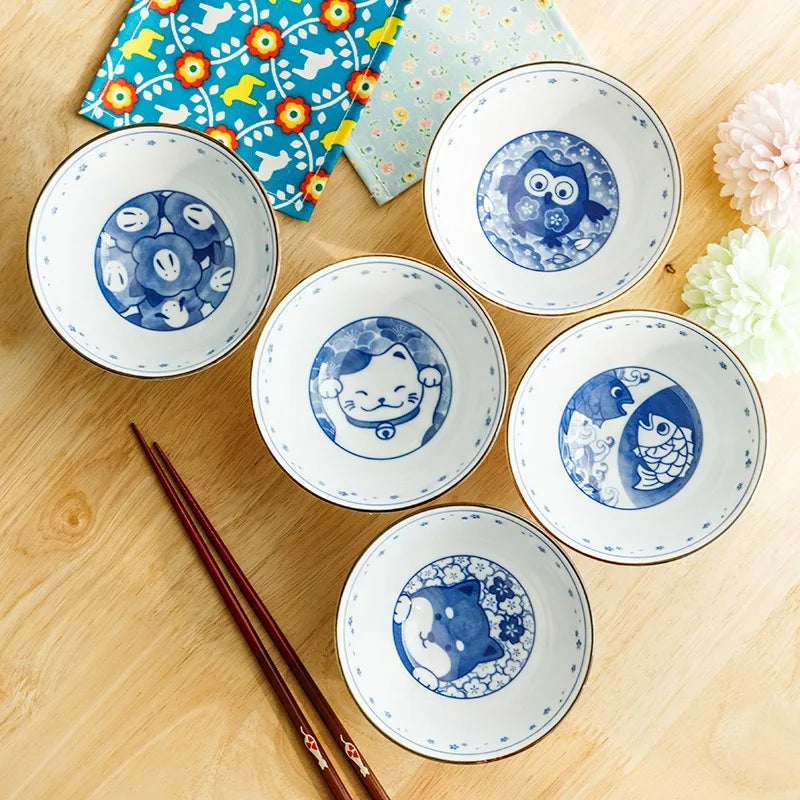 Set of five small ceramic kawaii bowls with blue animal designs on a wooden surface, accompanied by chopsticks.