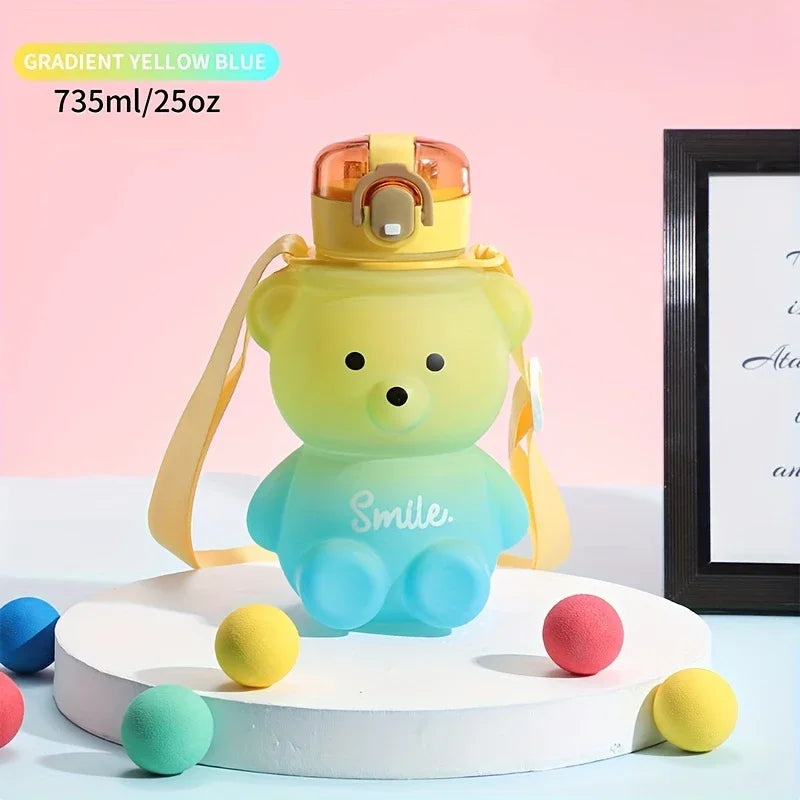 Gradient yellow to blue bear-shaped kawaii water bottle on a white platform with colorful balls against a pink background.