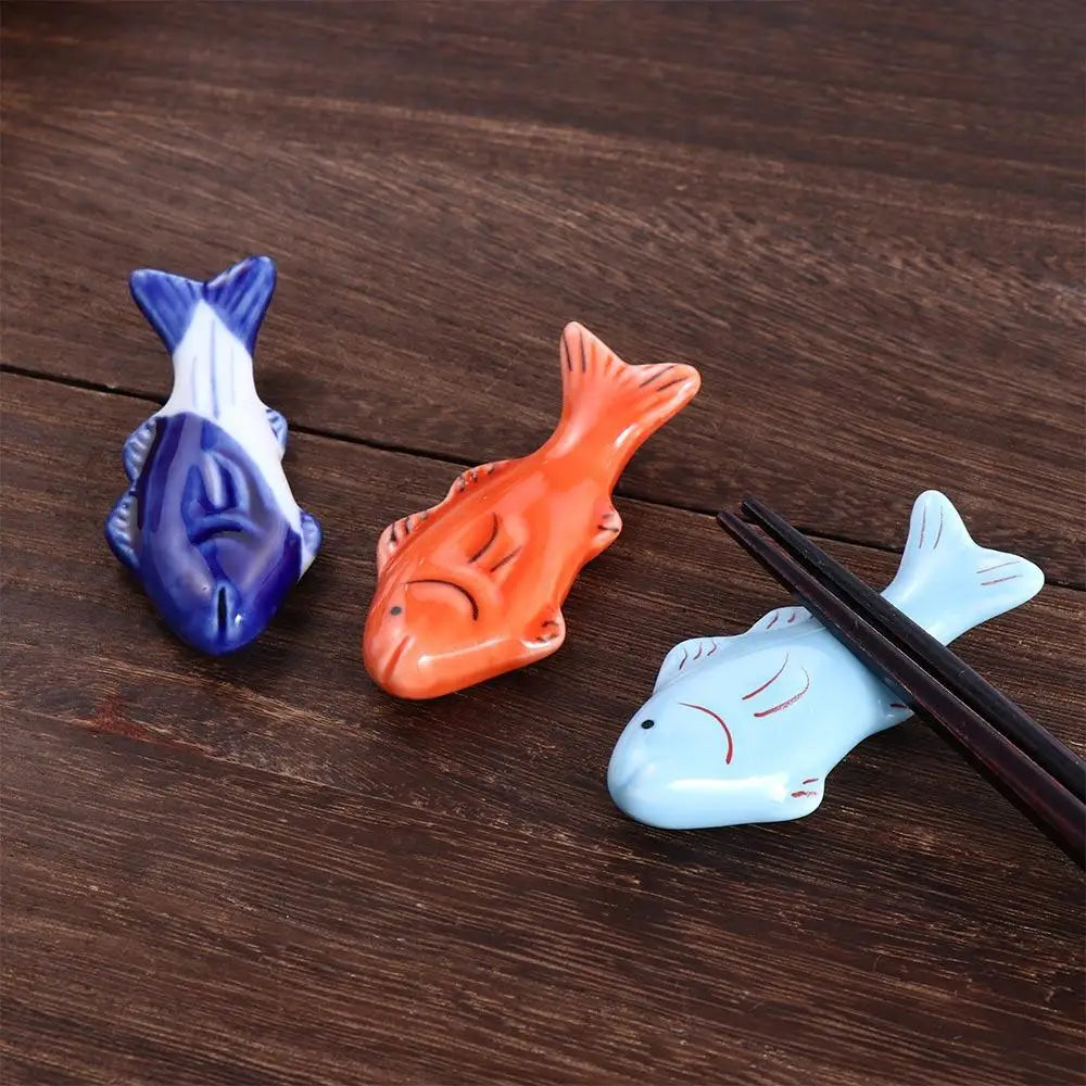 Three fish-shaped ceramic kawaii chopstick holders on a wooden surface with chopsticks.