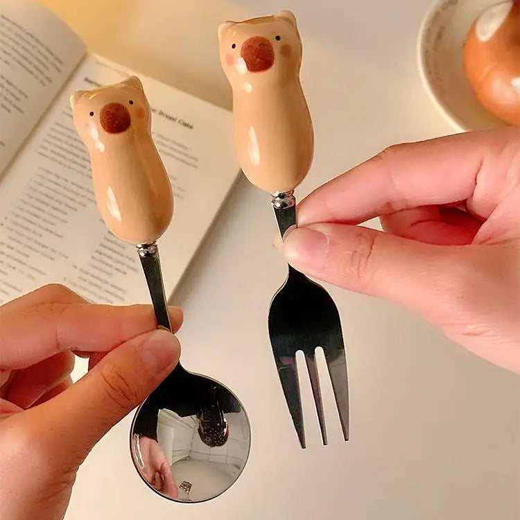 Kawaii utensils with bear handles held by a person, with a book in the background.