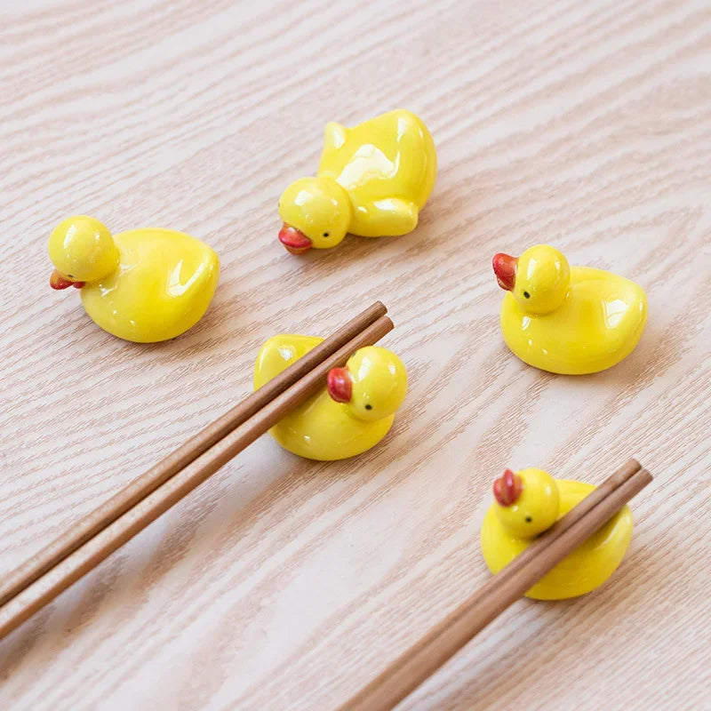 Yellow duck-shaped kawaii chopstick holders on a wooden surface with wooden chopsticks.