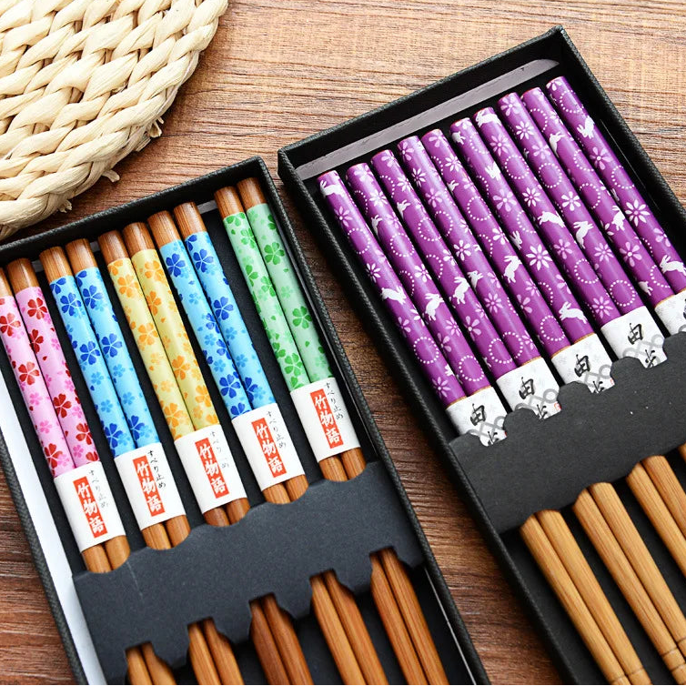 Colorful patterned kawaii chopsticks in black boxes on a wooden surface
