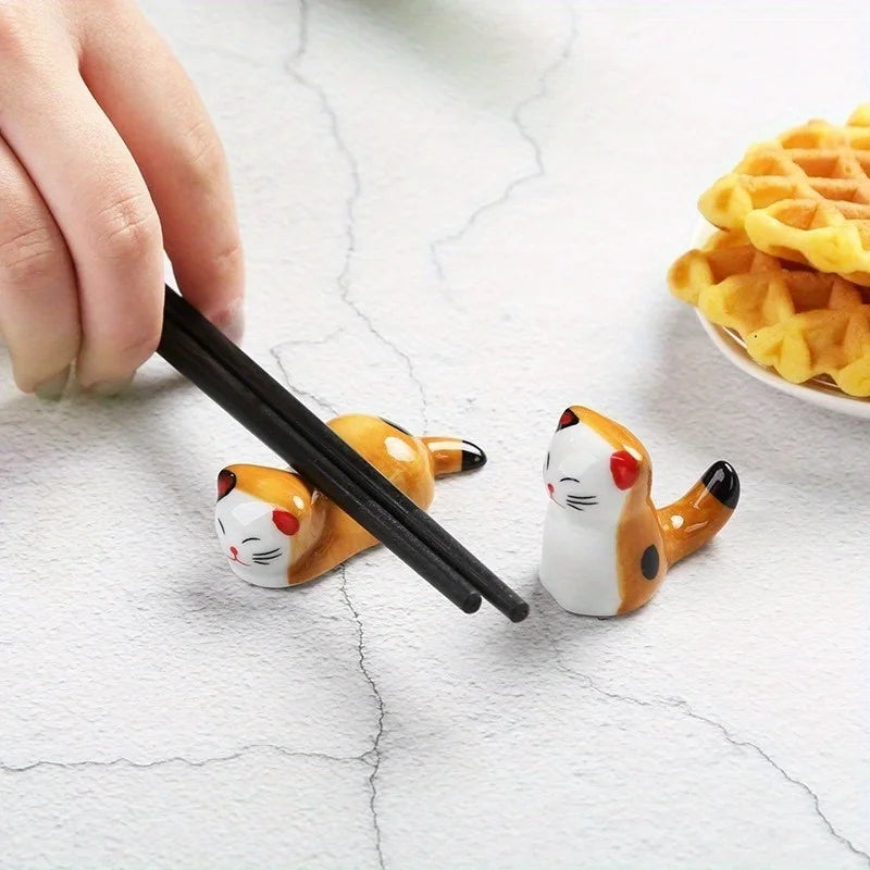Kawaii cat-shaped kawaii chopstick holder with a hand using black chopsticks on a light surface.