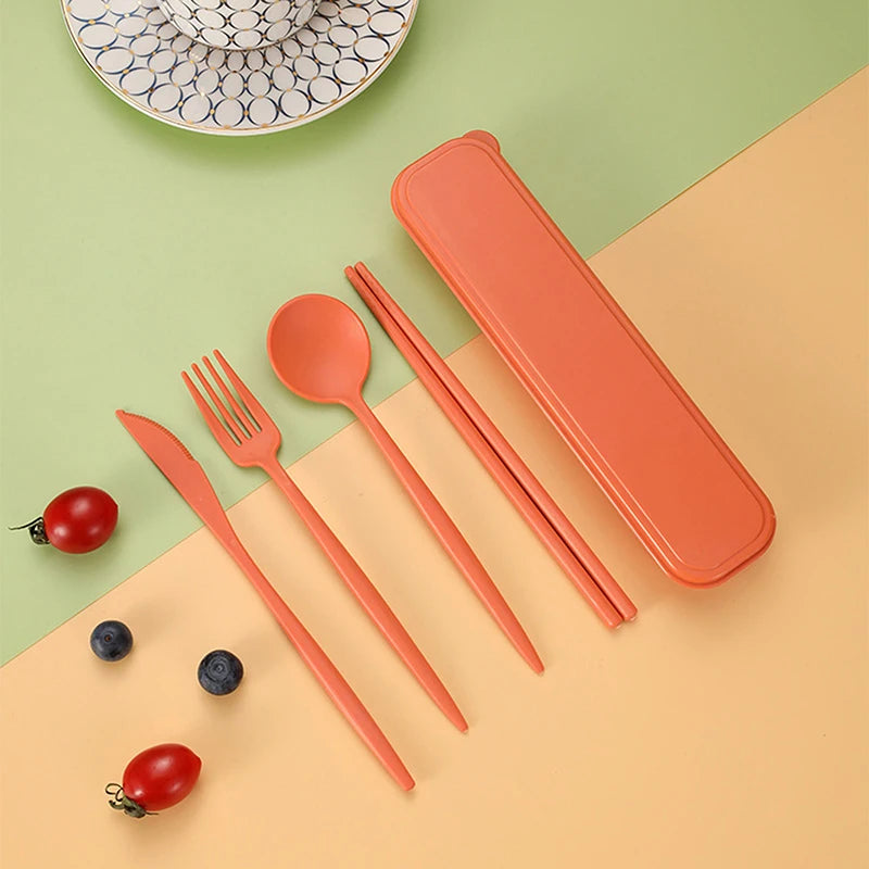 Set of orange kawaii cutlery including knife, fork, spoon, and chopsticks with a carrying case on a green and beige background.