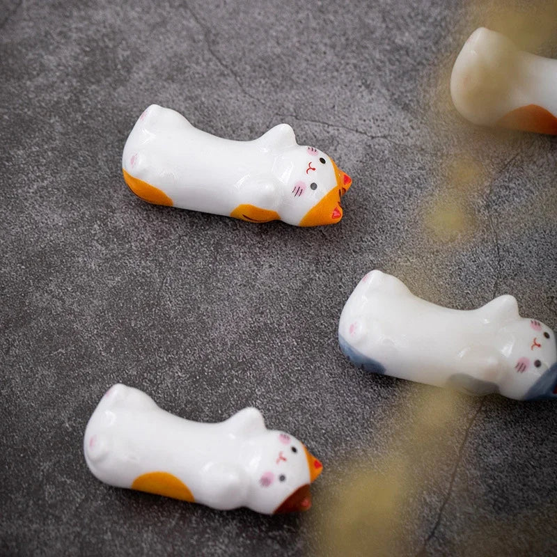 Three small cat-shaped kawaii chopstick holders on a gray surface