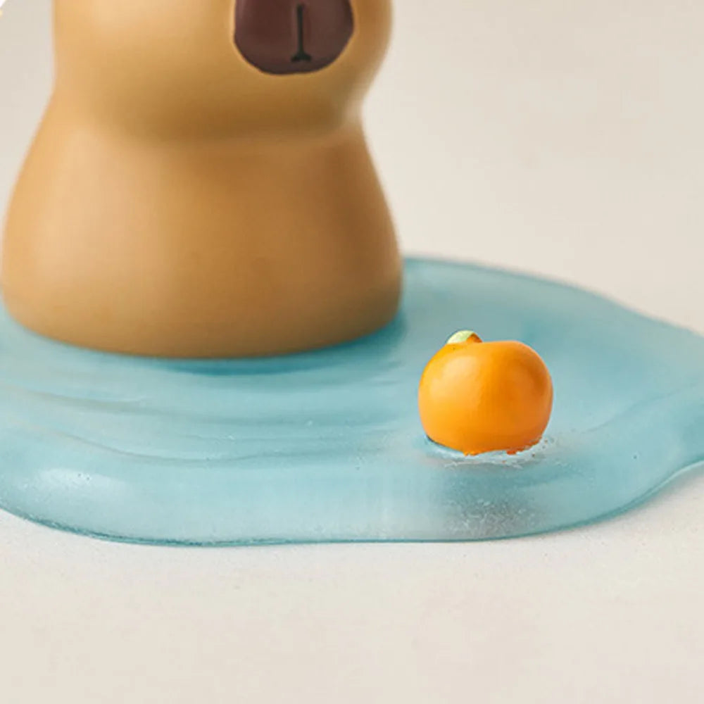Kawaii phone holder of a small orange fruit on a blue surface with a brown object in the background
