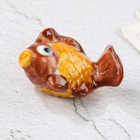 Ceramic fish-shaped kawaii chopstick holders with brown and yellow colors on a white marble surface