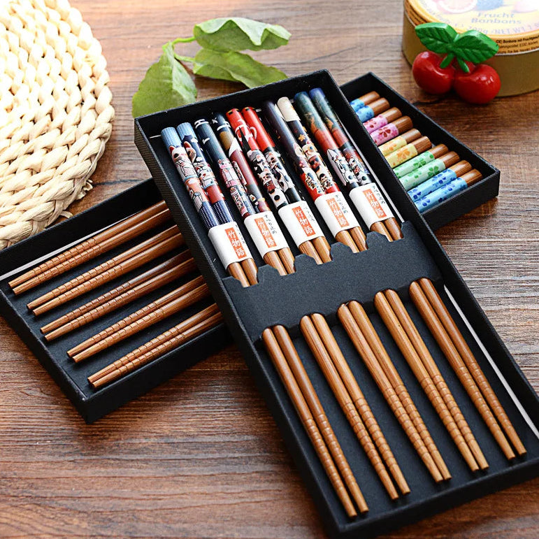 Set of wooden kawaii chopsticks in a black box on a wooden surface with decorative items.