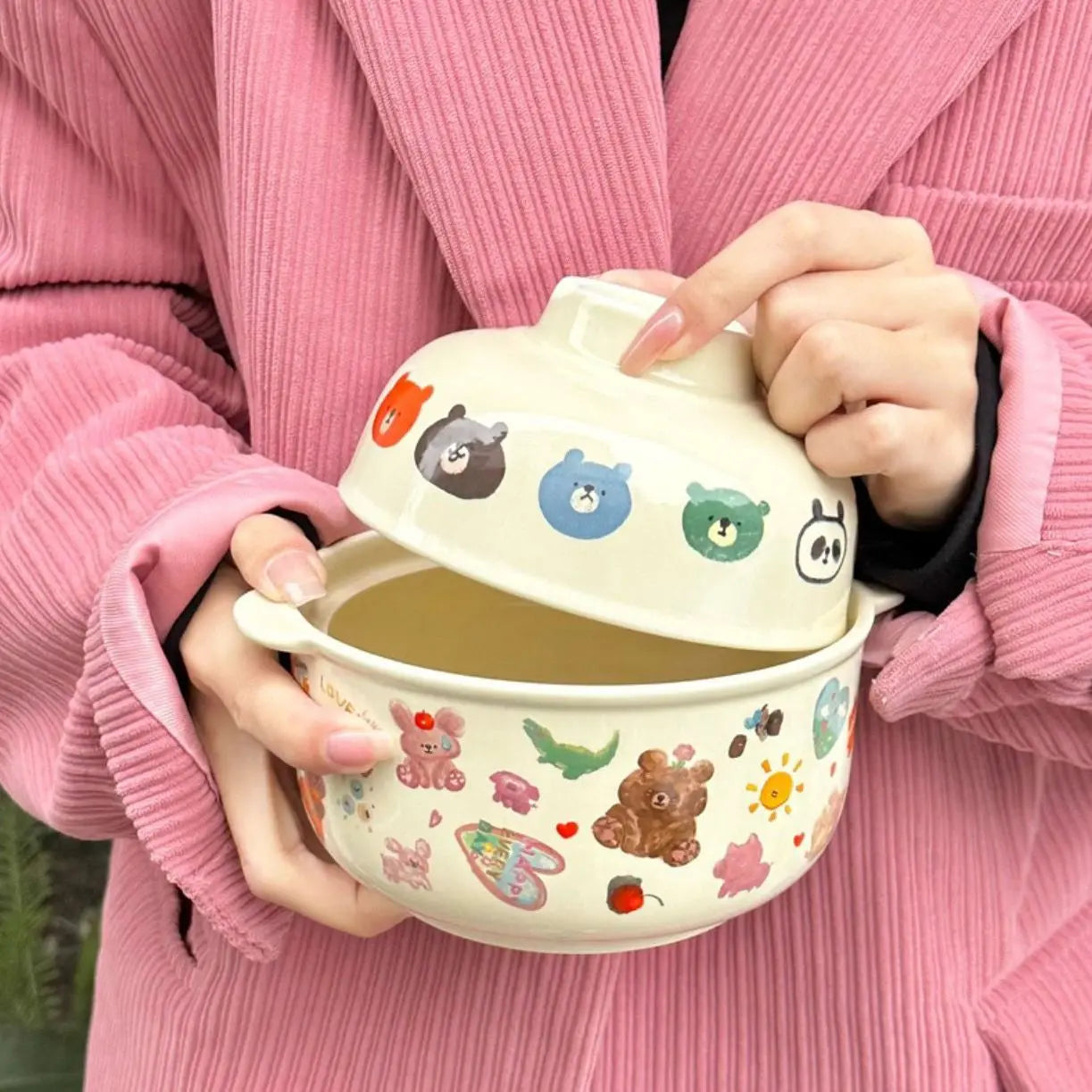 Person holding a cartoon-themed kawaii bowl with a lid, wearing a pink coat.