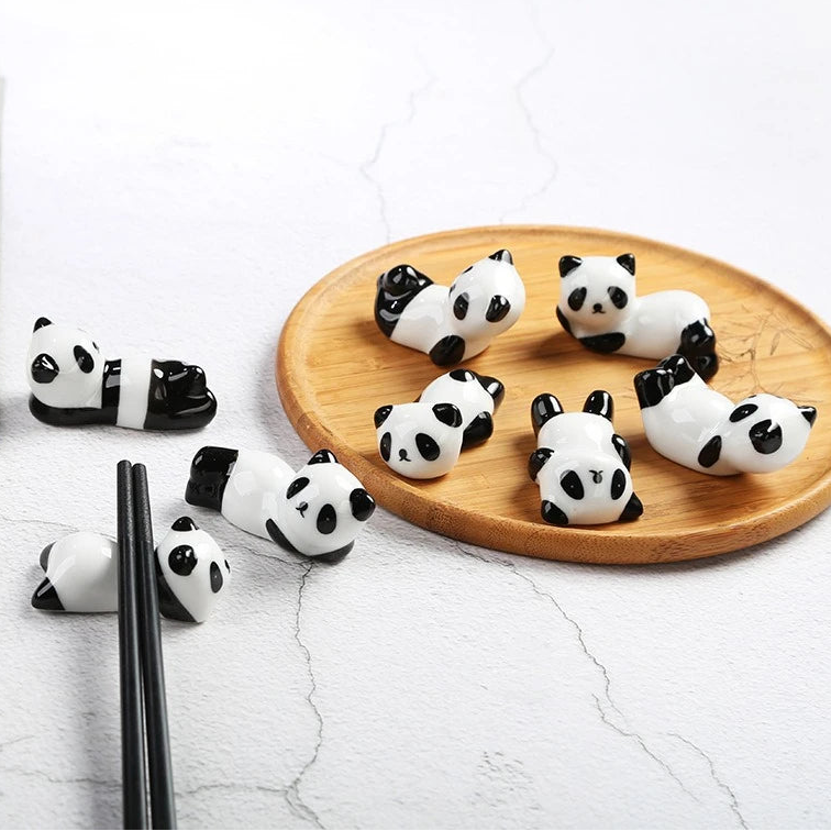 Panda-shaped kawaii chopstick holders on a wooden plate with chopsticks on a light gray background