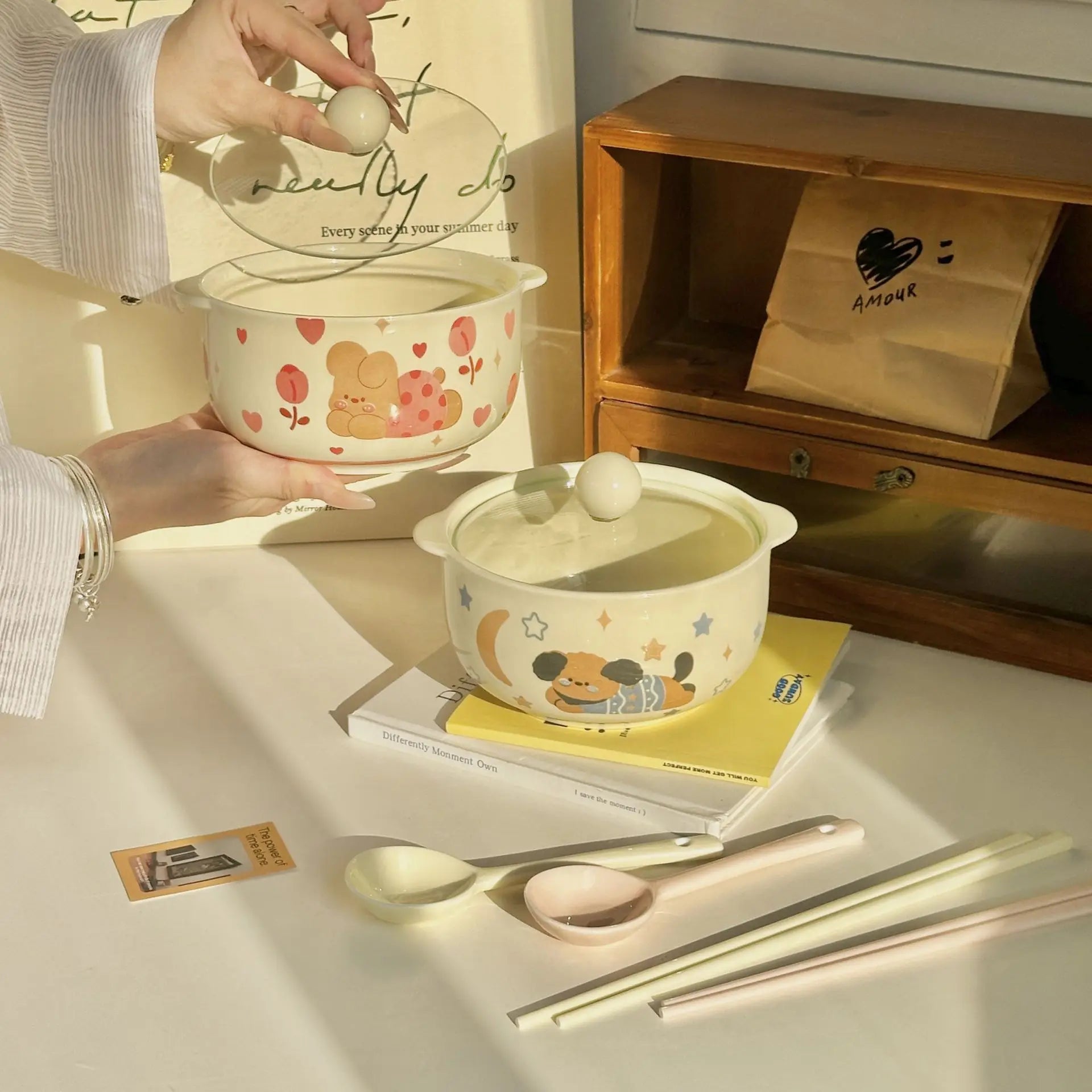 Ceramic kawaii ramen bowls with cartoon designs on a table with utensils and a wooden shelf in the background.