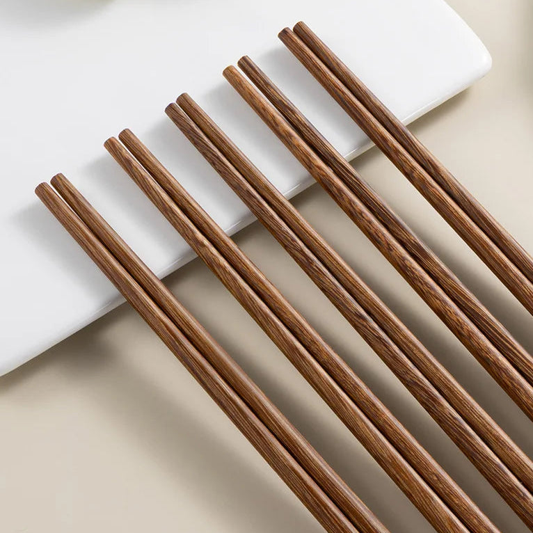 Set of wooden kawaii chopsticks on a light surface with a white plate and green apples in the background.