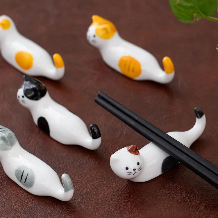 Cat-shaped ceramic kawaii chopstick holders on a brown surface with a leaf in the corner.