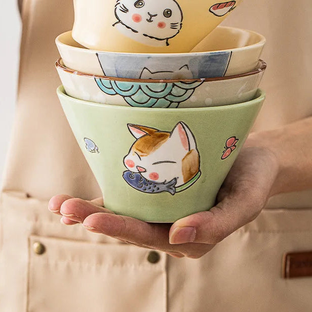 Stack of ceramic kawaii ramen bowls with cat illustrations held by a person