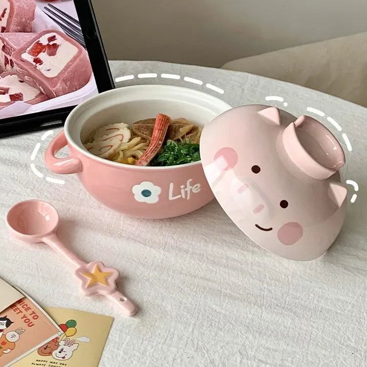 Pink cartoon-style kawaii ramen bowl with lid containing noodles, on a white surface.