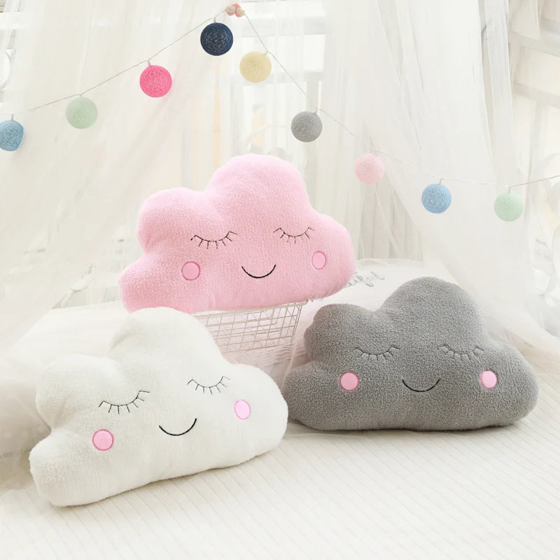 Three cloud-shaped kawaii pillows in pink, gray, and white with smiley faces on a light background.