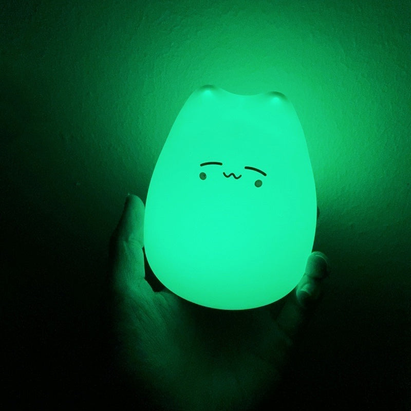 Green glowing night light with a kawaii face design held in a hand against a dark background