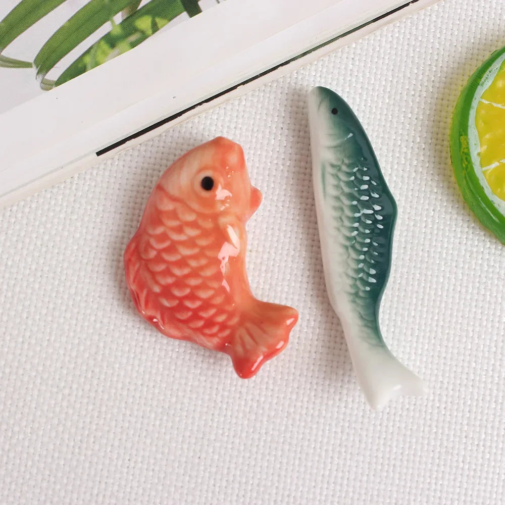 Two ceramic fish-shaped kawaii chopstick holders on a textured surface with a leaf in the corner.