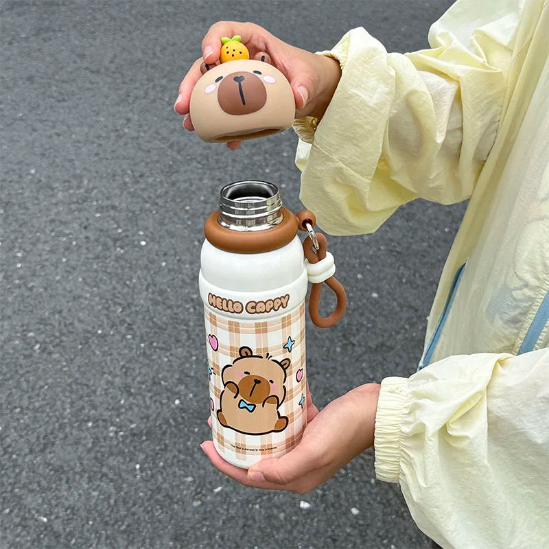 Person holding a cartoon-themed kawaii water bottle with a bear design on a gray pavement background