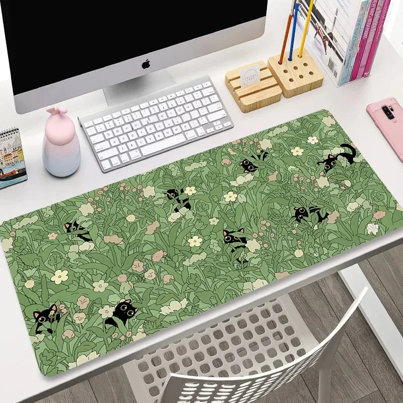 Desk setup with a green desk mat featuring Kawaii black cat and floral pattern, keyboard, and computer monitor.