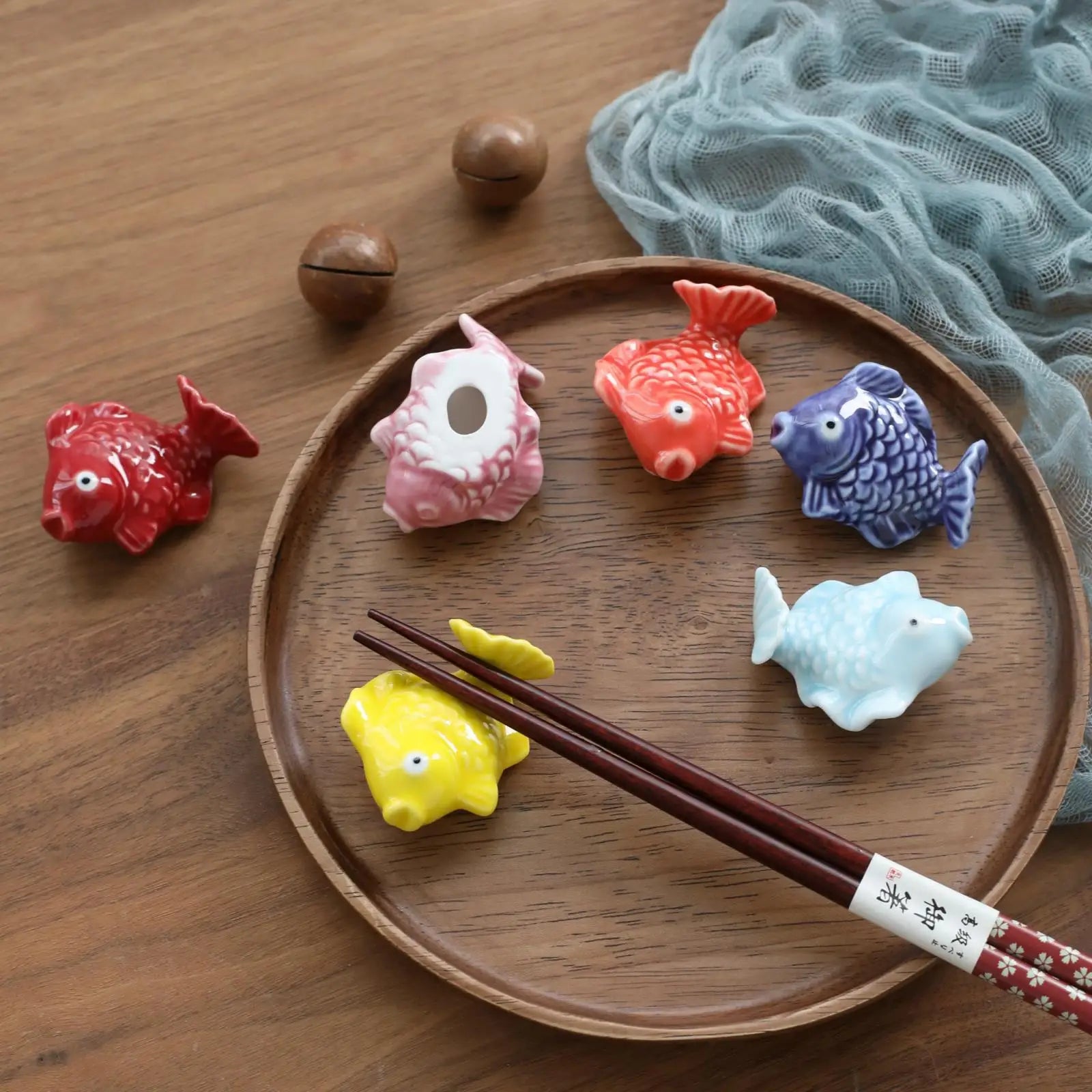 Colorful fish-shaped kawaii ceramic chopstick holders on a wooden plate with chopsticks.