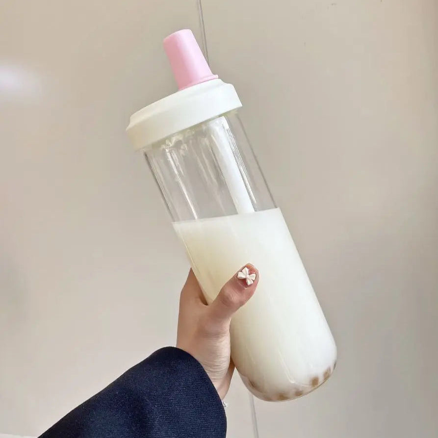 Hand holding a kawaii water bottle with a pink cap filled with a white liquid against a plain background