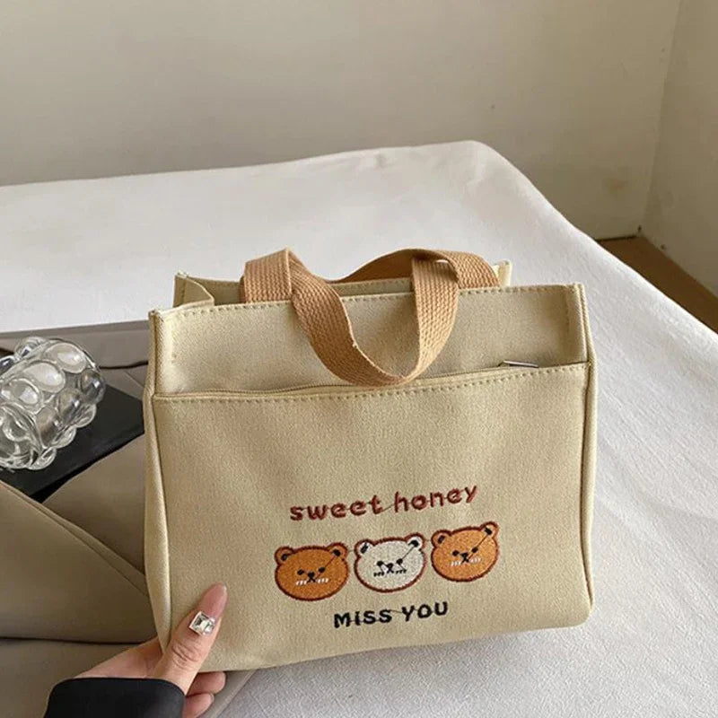 Beige kawaii tote bag with cartoon bears and text held by a hand on a light surface.