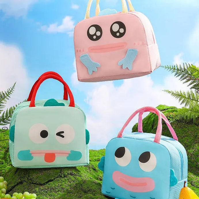Three cartoon-patterned kawaii lunch bags on a grassy background with a blue sky.