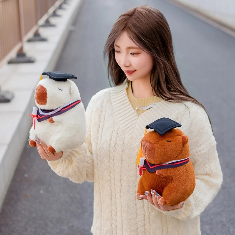 Woman holding two capybara plush toys resembling animals with graduation caps on a bridge.