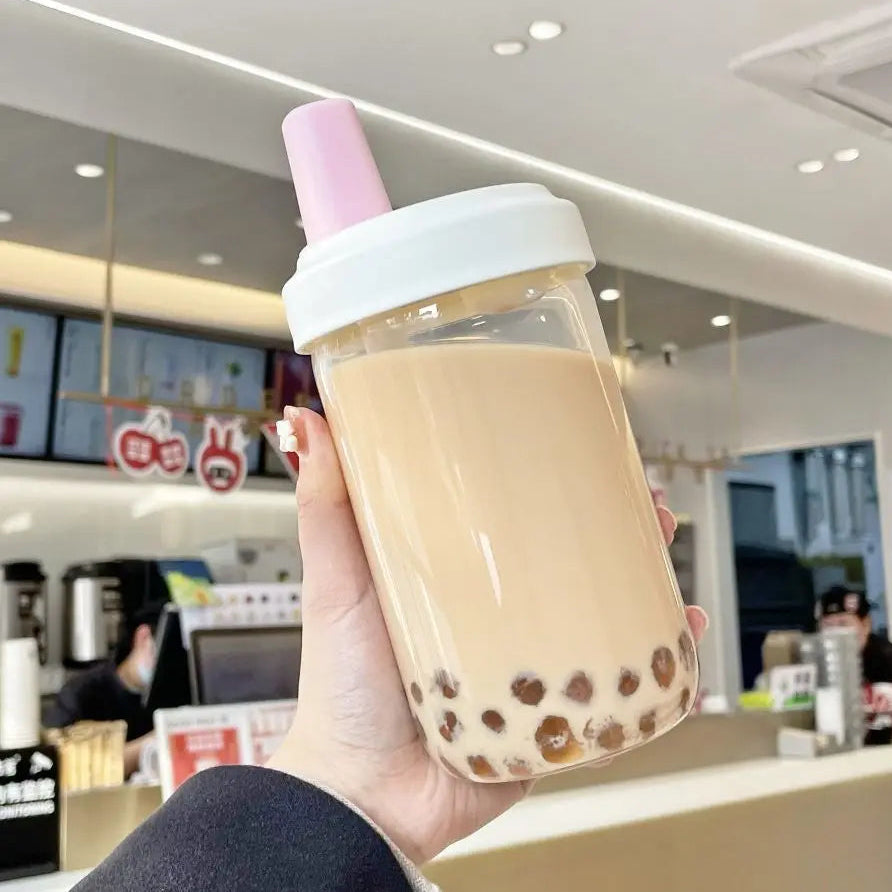Hand holding a clear kawaii cup with bubble tea in a cafe setting