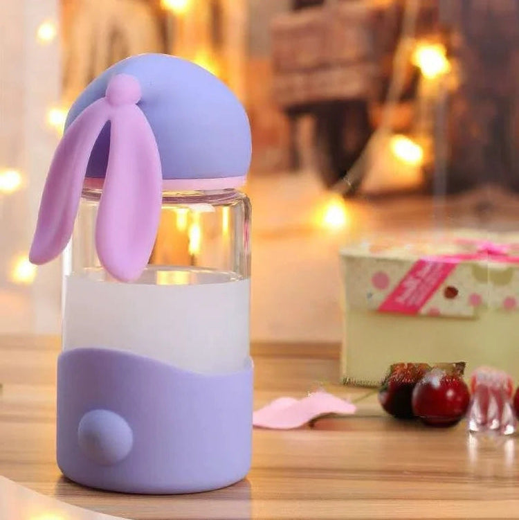 Kawaii water bottle with purple lid and ears on a wooden surface with blurred lights in the background