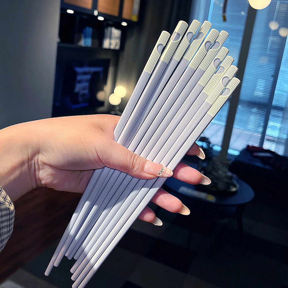 Hand holding a bundle of white kawaii chopsticks with gold patterns against a blurred indoor background