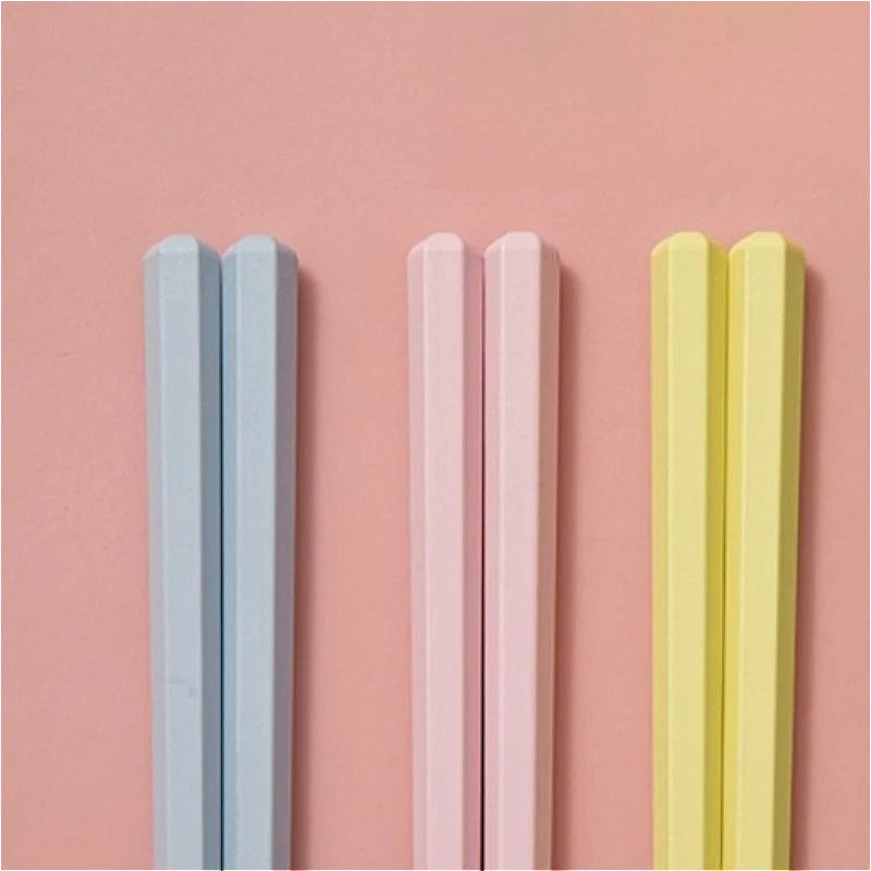 Three pairs of kawaii chopsticks in blue, pink, and yellow on a pink background