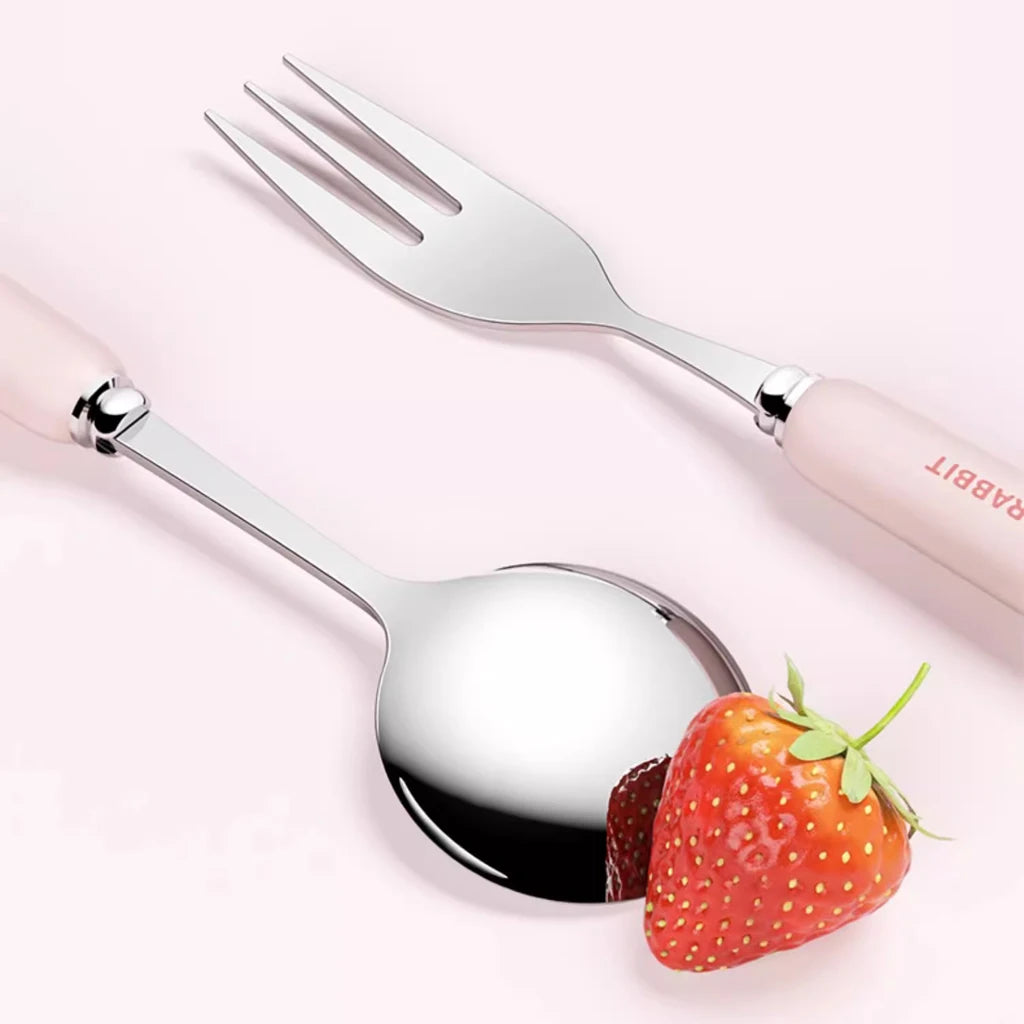 Kawaii utensils with pink handles next to a strawberry on a light pink background